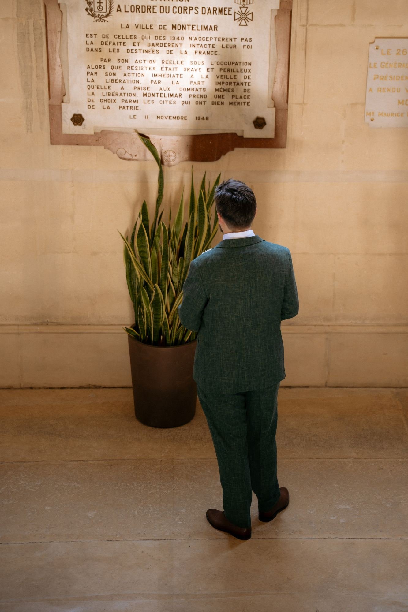 Le marié de dos devant une plaque commémorative